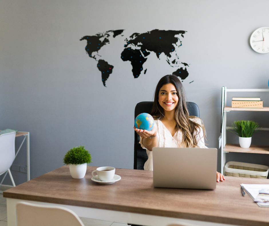 Una emprendedora frente al computador sosteniendo el mundo en una mano y el mapa a tras de ella 